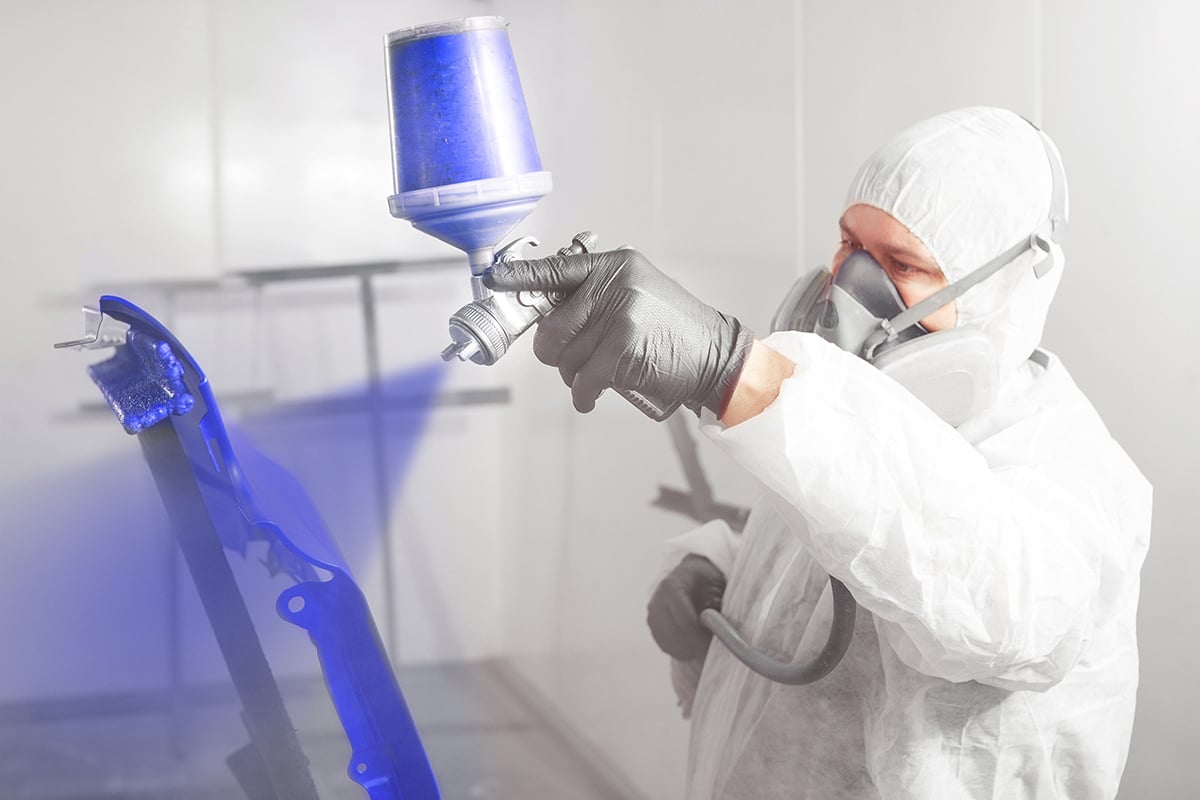 Car painter spraying paint on vehicle part