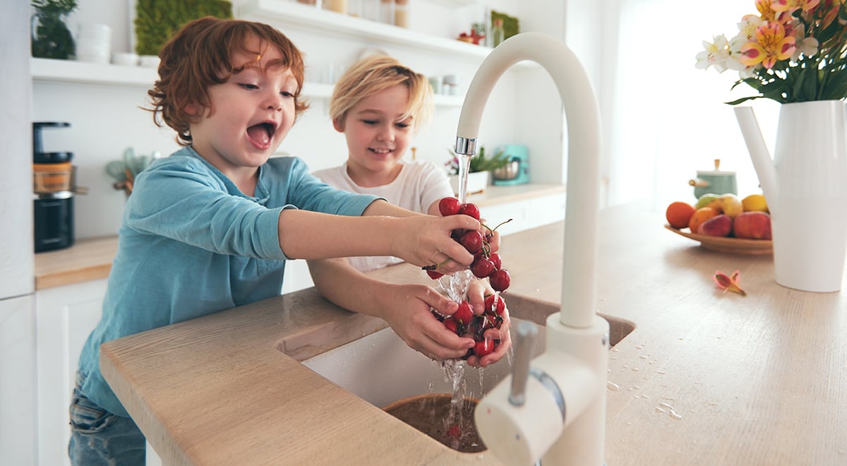 Happy children washing cherries with tap water in kitchen